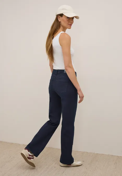 Frau mit weißem Top, dunkler Jeans und Kappe schaut über die Schulter.